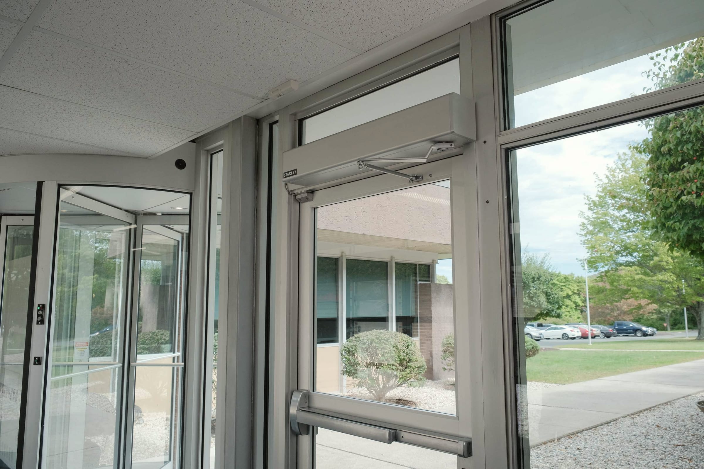 An automatic door operator in its housing, mounted along the top rail of an aluminum framed glass door.
