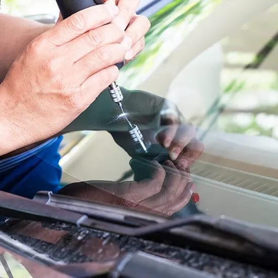 A technician’s hands injecting resin into a stone chip on a windshield.