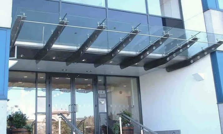 A frameless glass canopy carried on steel arms over the entrance of a modern commercial building.