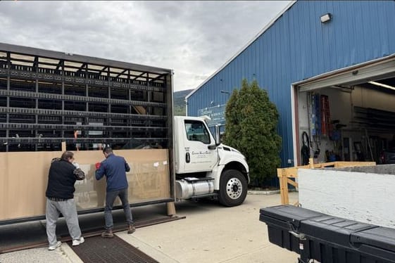 Two of the crew easing a crated glass shipment off a rack truck outside the shop's open bay door.