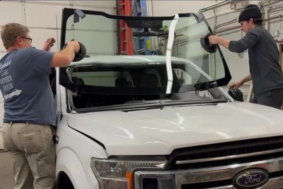 Two technicians lowering a windshield into a pickup inside the shop.