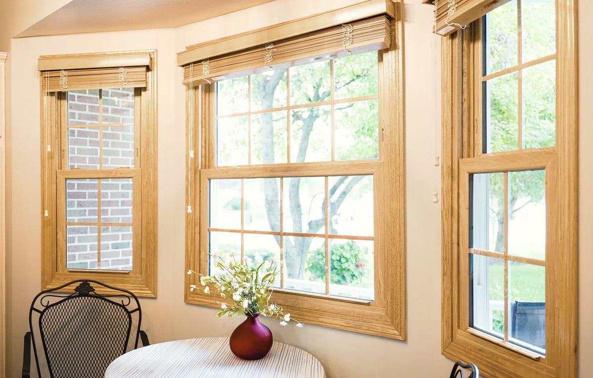A row of wood-framed windows with divided panes in a bright room, a small table and a vase of flowers in front.